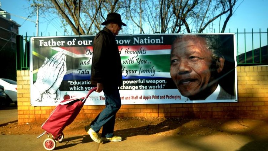 Un homme marche le 9 juillet 2013 devant une affiche sur laquelle figure une photo de Nelson Mandela, accrochée sur la grille du MediClinic Heart Hospital de Pretoria