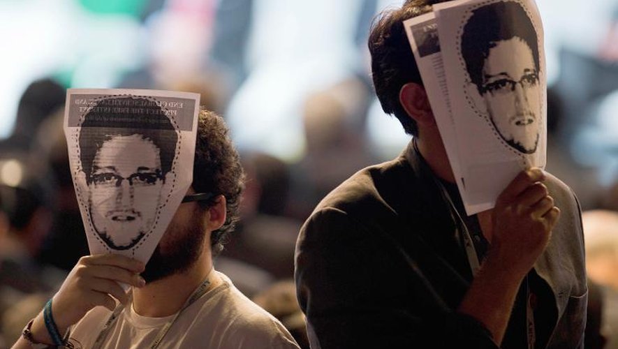 Des manifestants tiennent devant leur visage une photo de l'ex-consultant américain Edward Snowden, à l'origine du scandale des écoutes de la NSA, pendant la cérémonie d'ouverture du sommet NETmundial, le 23 avril 2014 à Sao Paulo