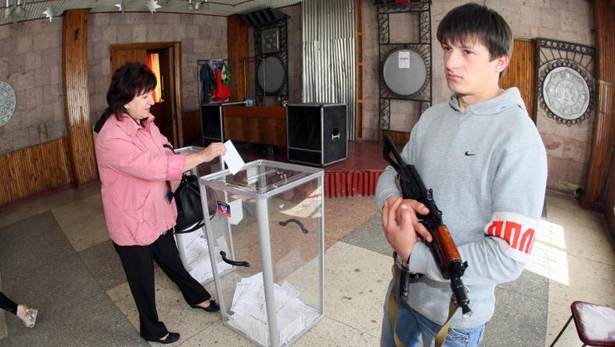 Des activistes prorusses gardent un bureau de vote à Donetsk en Ukraine, alors qu'une femme dépose son bulletin lors du référendum organisé par les rebelles