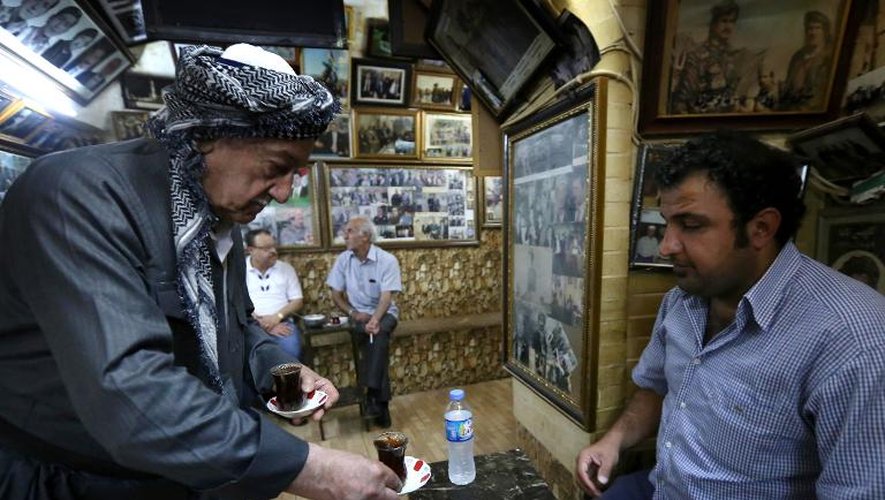 Mam Khalil, 76 ans, sert un client de son café, le 12 mai 2014 à Erbil, la capitale de la région autonome kurde du nord de l'Irak, devant les galeries de photos retraçant l'histoire du pays qui tapissent les murs