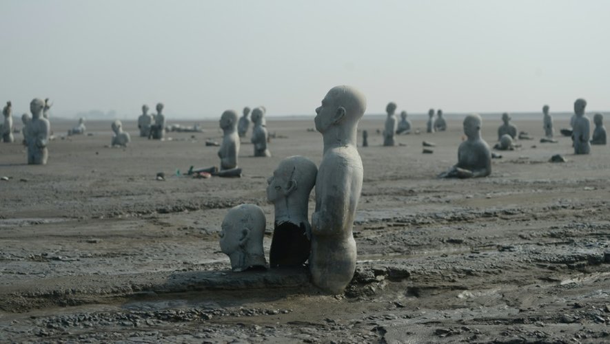 Vue en date du 28 mars 2016 de sculptures de personnes à moitié enterrées dans le volcan de boue qui a surgi de terre le 29 mai 2006 à Sidoarjo