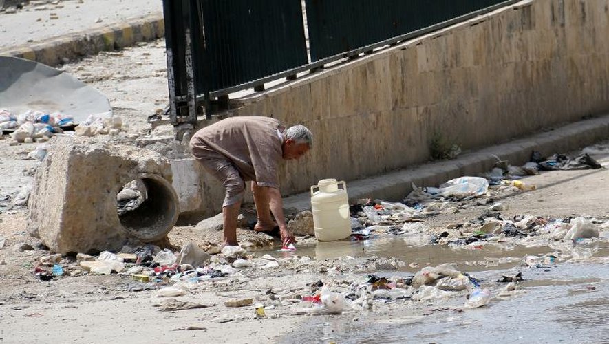 Un homme lave quelque chose dans une flaque d'eau stagnante à Alep, le 12 mai 2014