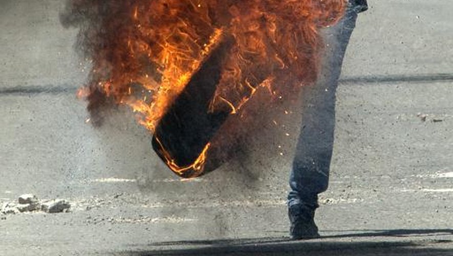 Un Palestinien donne un coup de pied dans un pneu en feu lors d'affrontements avec l'armée israélienne, lors du 66e anniversaire de la "Nakba", l'exode des réfugiés au moment de la création d'Israël en 1948, le 15 mai 2014 à Kalandia,