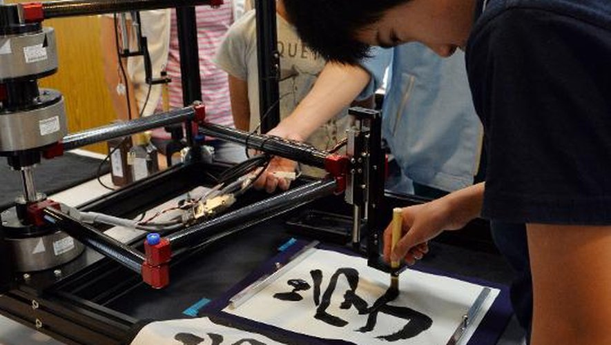 Un jeune garçon s'essaye à la calligraphie grâce à un "robot", le 30 juillet 2013 à l'université de Keio, à Yokohama, dans les environs de Tokyo