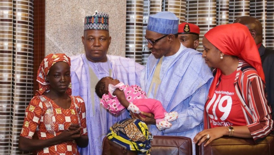 Le président du Nigeria Mohammadu Buhari tient l'enfant d'Amina Ali (g), la première des 219 lycéennes de Chibok kidnappées par Boko Haram à avoir été retrouvée, le 19 mai 2016 à Maiduguri
