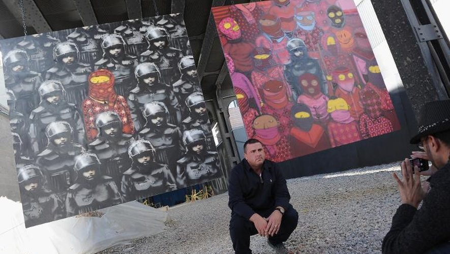 Un homme pose devant des oeuvres de l'artiste britannique de rue Banksy, le 18 octobre 2013 à New York
