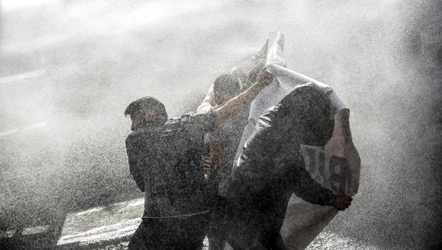 Des manifestants turcs s'abritent, derrière une bannière, des canons à eau que la police anti-émeute utilise pour les disperser , le 22 mai 2014, à Istanbul