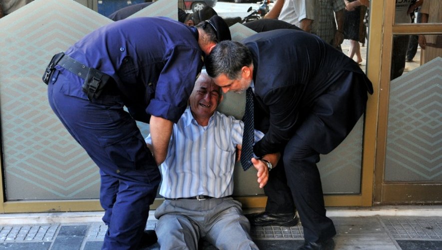 Giorgos Chatzifotiadis, 77 ans, est aidé par un employé de la banque et un policier alors qu'il pleure devant l'établissement, le 3 juillet 2015 à Thessalonique