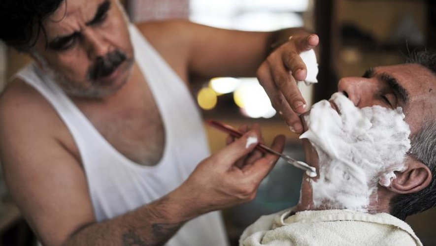 Un barbier turc Mehmet Haskan (g) rase un client dans son salon le 19 juillet 2013 à Istanbul
