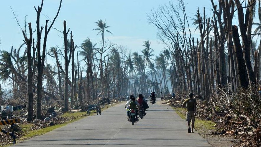 Des motocyclistes sur une route de Baganga aux Philippines au milieu d'arbres détruits par un typhon le 11 décembre 2012