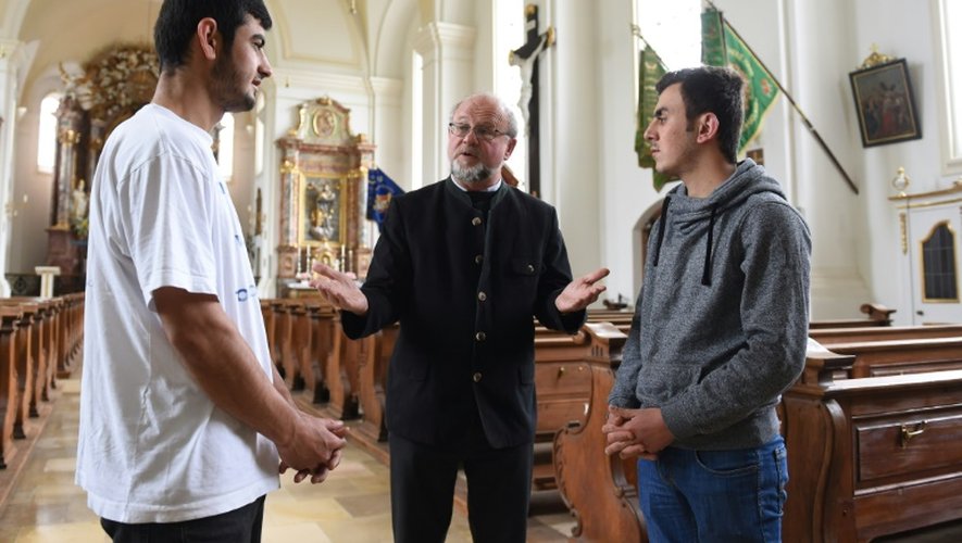 Le pasteur Peter Brummer s'entretient avec des migrants Peshtiwan Nasser Abdal (g) et  Suud-iazdxn Arab (d), dans l'église Saint Joseph de Tutzing (sud de l'Allemagne), le 24 mai 2016