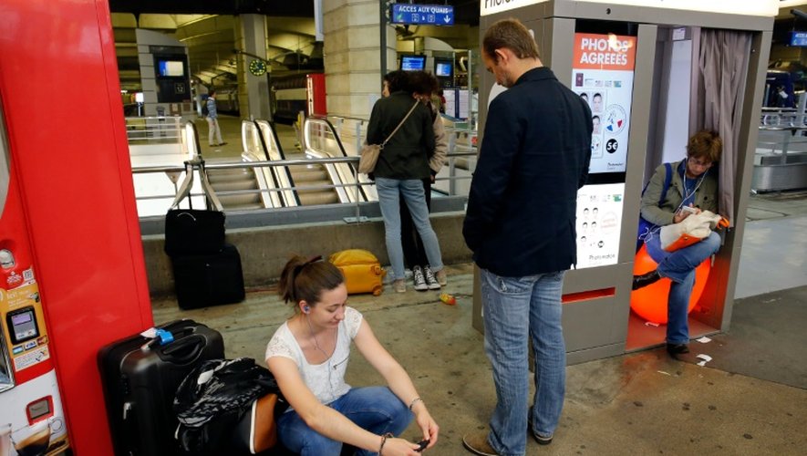 Des voyageurs assis par terre ou dans une cabine de photos d'identité, le 29 mai gare Montparnasse à Paris