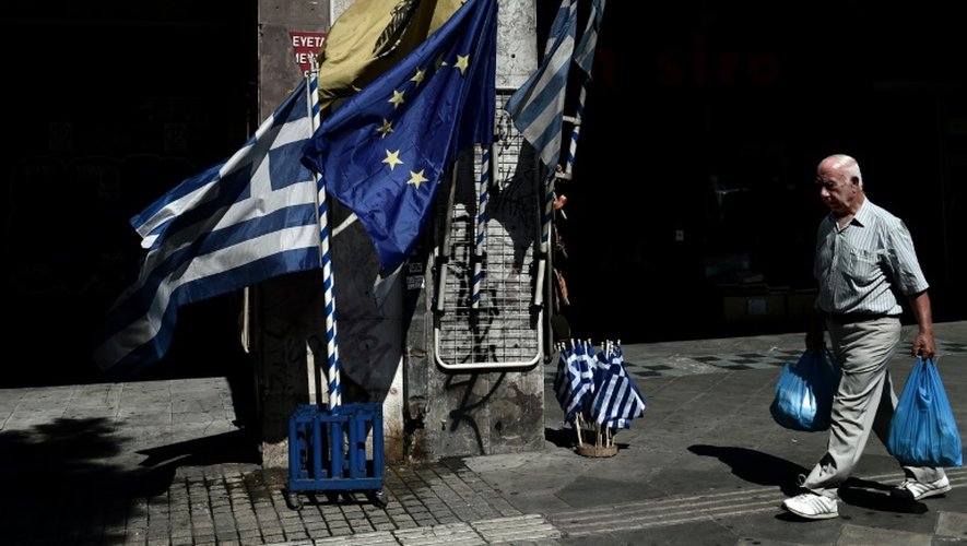 Un homme passe devant des drapeaux grecs et une bannière européene dans une rue du centre d'Athènes, le 13 juillet 2015