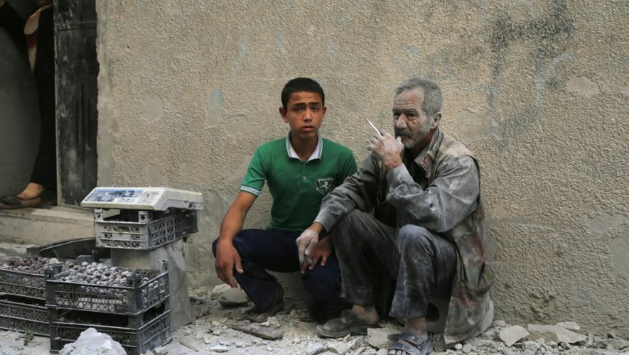 Deux hommes assis dans une rue après un raid aérien attribué aux troupes du régime dans le quartier de Sukkari, sous contrôle rebelle, à Alep, le 30 mai 2016