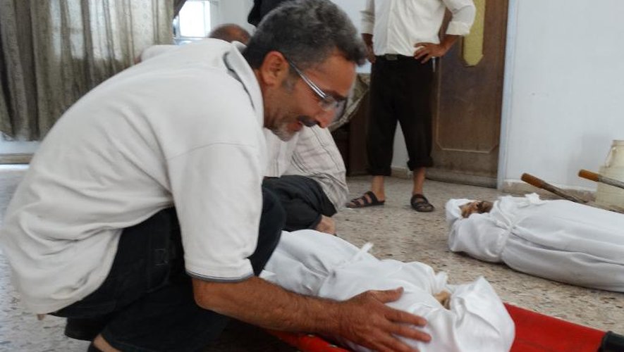 Photo fournie par le réseau d'opposition syrienne Shaam News montrant un homme devant les corps de victimes  d'une attaque chimique, le 23 août 2013 près de Damas