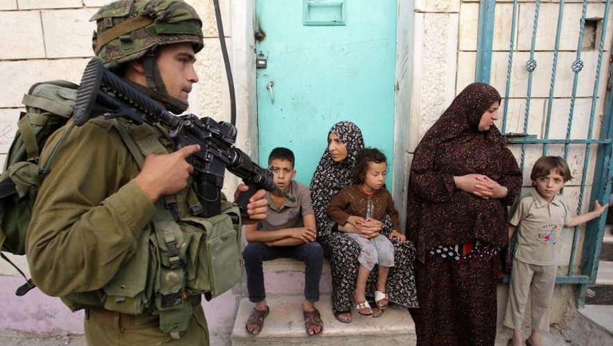 Soldat israélien passant devant des Palestiniens dans le village de Tafoh, près d'Hébron, en Cisjordanie, le 15 juin 2014