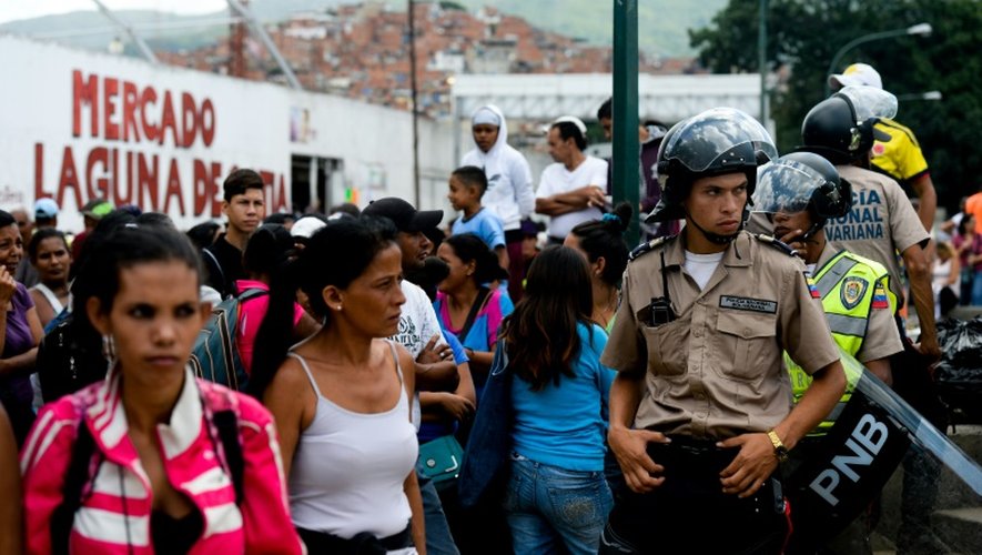 Des policiers surveillent les personnes qui font la queue pour acheter des victuailles à l'extérieur d'un supermarché à Caracas, le 11 juin 2016