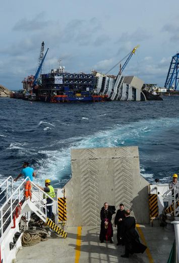 Des hommes d'église sur un ferry, à proximité de l'épave du navire de croisière Costa Concordia, échoué en janvier 2012 près de la petite île toscane du Giglio, le 15 septembre 2013