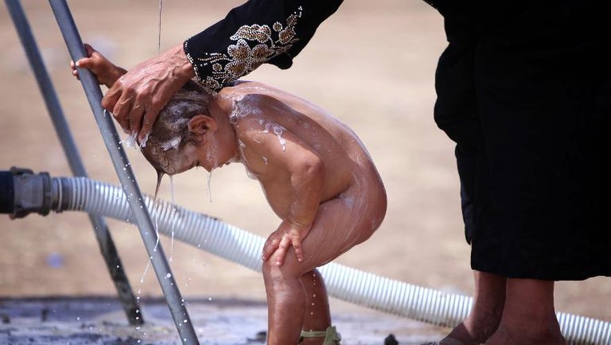 Une mère qui fait partie des milliers de personnes ayant fui les violences du nord de l'Irak tente de laver son enfant au camp de réfugiés d'Aski Palak, près d'Arbil, le 13 juin 2014