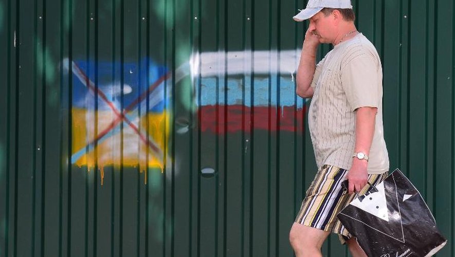 Un habitant de Slaviansk passe devant des graffitis, un drapeau ukrainien barré et un drapeau russe, le 24 juin 2014