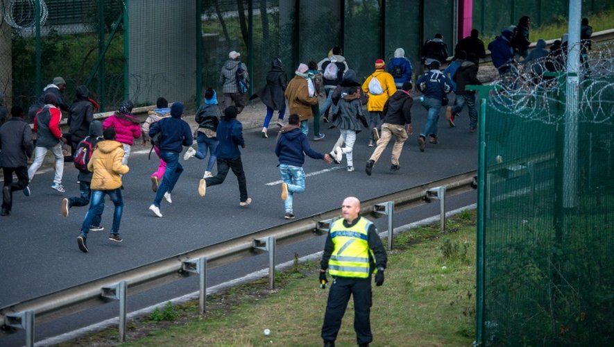 Des migrants tentent de passer le tunnel sous le regard d'un policier, le 29 juillet 2015 à Coquelles, près de Calais