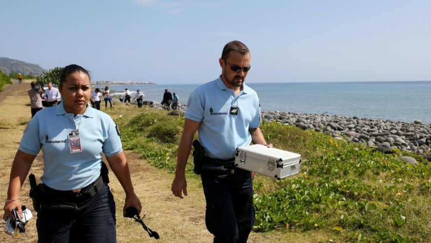 Des policiers portent dans une boîte des débris métalliques découverts sur une plage de Saint Denis, à La Réunion, le 2 août 2015