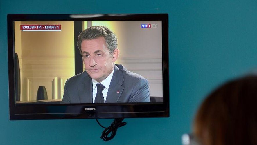 Une femme regarde Nicolas Sarkozy lors de son intervention télévisée pré-enregistrée, le 2 juillet 2014 à Paris
