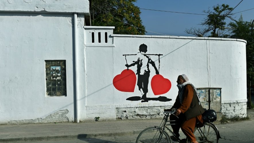 Un homme passe en vélo devant une peinture d'artiste réalisée sur un mur de Kaboul dans le cadre d'une campagne contre la corruption, le 24 juillet 2015