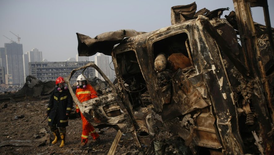 Des pompiers passent le 15 août 2015 devant un camion carbonisé par les explosions qui ont ravagé le port de Tianjin, dans l'est de la Chine