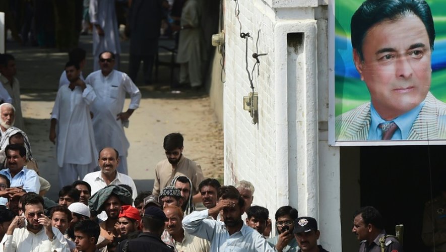 Des habitants du village pakistanais de Shadi Khan observent le 16 août 2015 les opérations de secours sous le portrait du ministre de l'Intérieur de la province du Pendjab Shuja Khanzada, mort dans un attentat suicide pendant un meeting politique