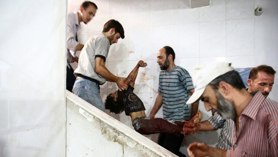 Des hommes transportent un enfant blessé par des frappes aériennes du régime dans un hôpital de fortune installé à Douma, ville tenue par les rebelles à 13km de Damas, le 16 août 2015