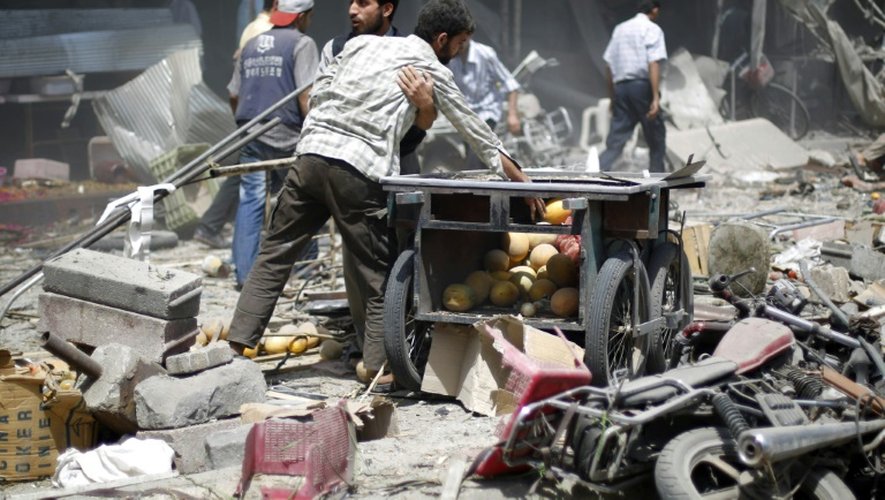 Des Syriens dans les décombres après des frappes aériennes menées par les forces gouvernementales contre un marché de Douma, tenue par des rebelles, le 16 août 2015