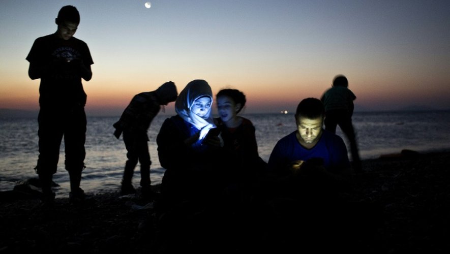 Des migrants regardent leur téléphone portable après avoir atteint l'île grecque de Kos, le 12 août 2015