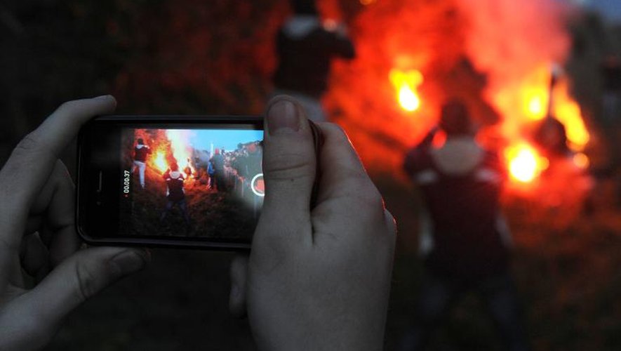 Un homme filme à l'aide de son téléphone portable des manifestants en train d'incendier un radar routier, à Jugon-les-Lacs, le 9 novembre 2013