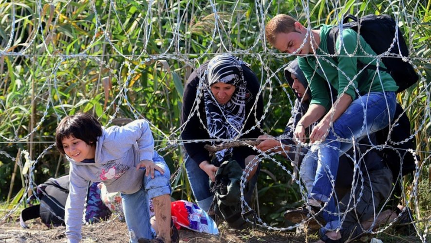 Une famille de migrants franchit une clôture de barbelés le 28 août 2015 à Roszke à la frontière entre la Hongrie et le Serbie