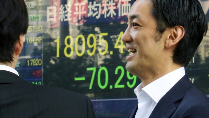 Des hommes d'affaires discutent devant des écrans de cotation à Tokyo le 2 septembre 2015