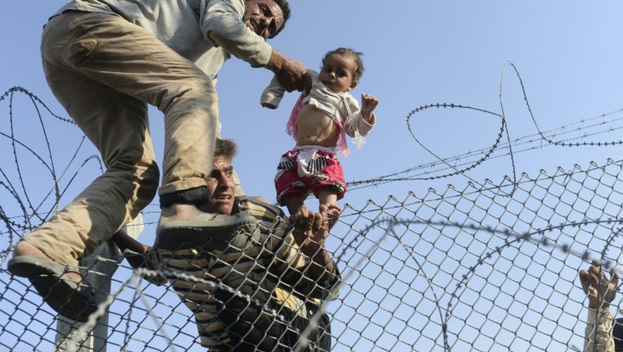 Photo prise le 14 juin 2015 par le photographe de l'AFP Bülent Kiliç, récompensé du Visa d'Or News à Perpignan, montrant 
un enfant syrien fuyant la guerre porté à bout de bras de l'autre côté de des barbelés en territoire turc au point de passage d'Akcakale dans la province de Sanliurfa