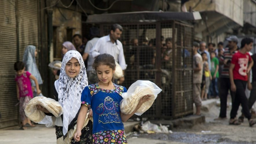 Deux jeunes filles portent des sacs de pain devant une boulangerie à Alep le 12 juillet 2016