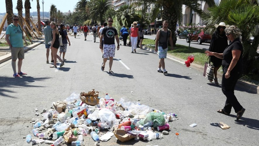 Sous le message "Lâche!" dessiné à la craie, des gens jettent des détritus le 18 juillet 2016 sur la promenade des Anglais à Nice, où un homme conduisant un camion a tué plus de 80 personnes le 14 juillet