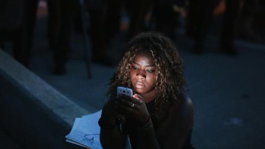 Une participante à la manifestation dénonçant la mort d'un jeune Noir tué par un policier blanc regarde son téléphone, alors que la police veille à proximité la 13 août 2014