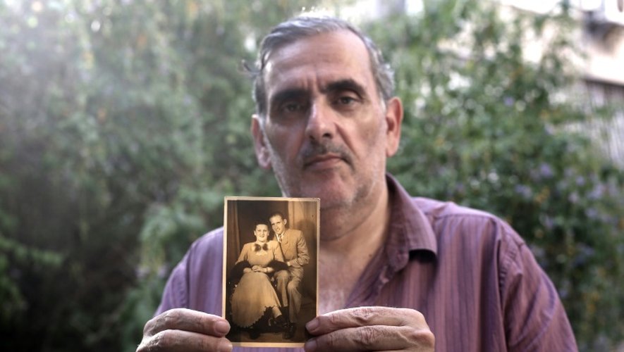 Gili Grunbaum, 60 ans, d'origine tunisienne, pose avec un portrait de ses parents adoptifs le 6 juillet 2016 à Ramat Gan près de Tel Aviv