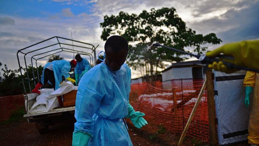 Un membre des services publics de fossoyeurs en Sierra Leone est aspergé de désinfectant tandis que des collègues chargent un camion des corps de victimes du virus Ebola, à Kailahun, le 14 août 2014