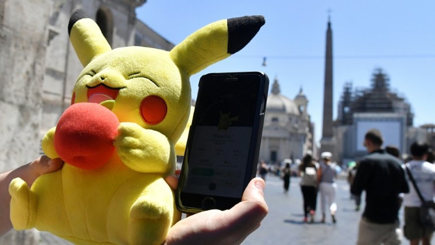 Un joueur tient une mascotte de Pokémon et joue au Pokémon Go sur son portable, le 19 juillet 2016 à Rome.