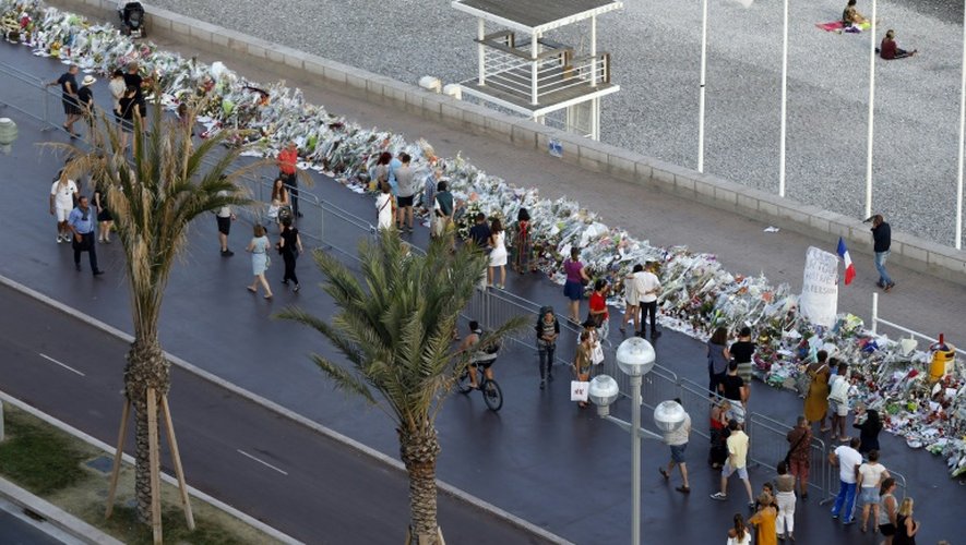 Des gens marchent près des fleurs et messages laissés à la mémoire des victimes à Nice le 20 juillet 2016