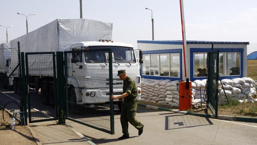 Un homme ouvre la grille du poste de douane au convoi de camions transportant de l'aide humanitaire le 22 août 20 à Izvarino à la frontière russo-ukrainienne