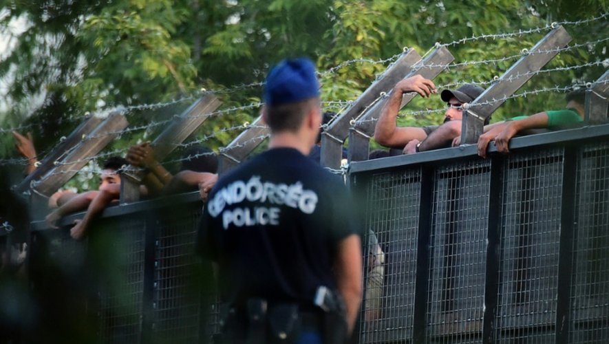 Des policiers hongrois surveillent des migrants qui se hissent sur la porte métallique qui ferme la frontière avec la Serbie, près de Röszke, le 15 septembre 2015