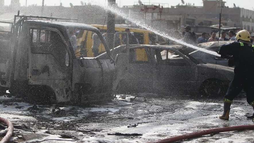 Un membre des services d'urgence éteint les fumées après un attentat à la voiture piégée le 26 août 2014 à Bagdad (Irak)