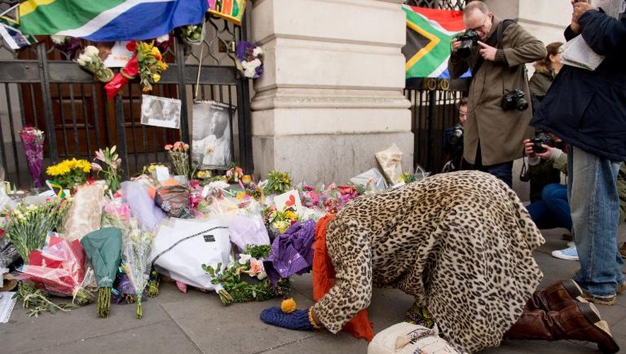 Une femme s'agenouille devant des fleurs déposées en hommage à Nelson Mandela devant l'ambassade d'Afrique du Sud à Londres, le 6 décembre 2013