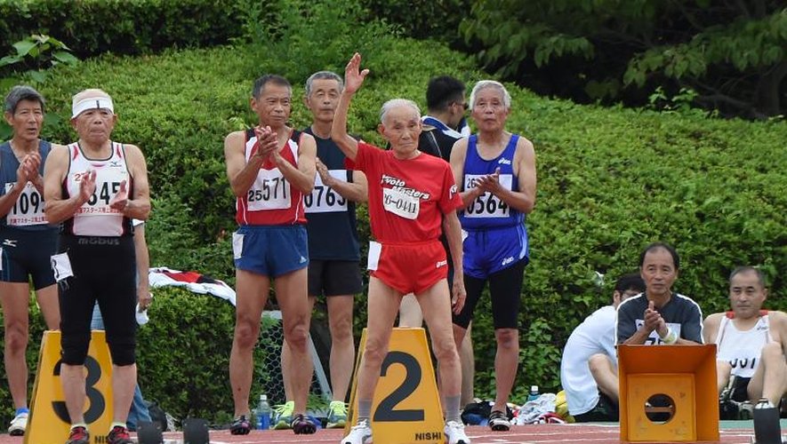 Hidekichi Miyazaki (c) lève la main lorsqu'il se place dans son couloir pour disputer le 100 mètres lors d'une compétition d'athlétisme pour seniors à Kyoto