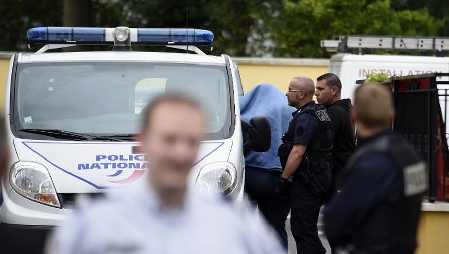 Un homme caché sous une couverture est amené dans une véhicule de police devant l'hôtel où trois personnes ont été retrouvées mortes le 28 août 2014 à Draveil